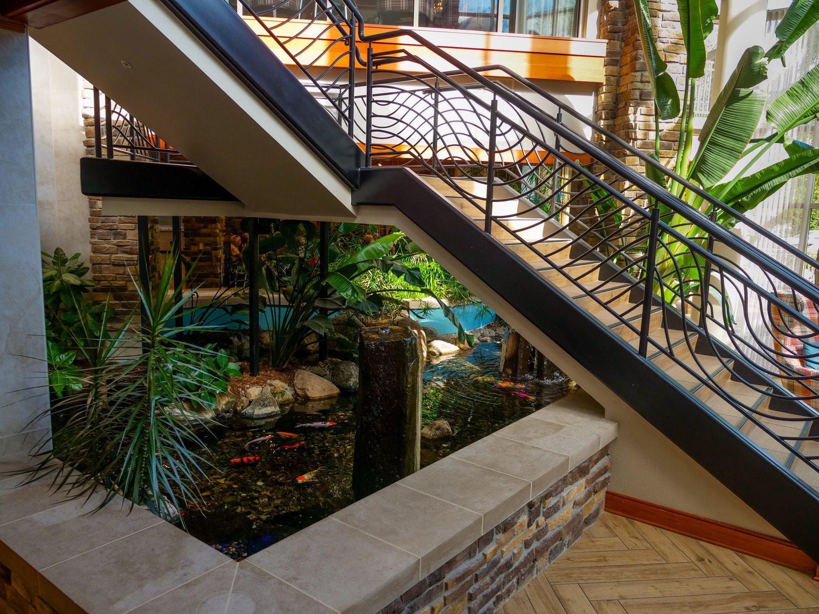 Indoor koi pond with a stone waterfall column viewed from a staircase inside a home