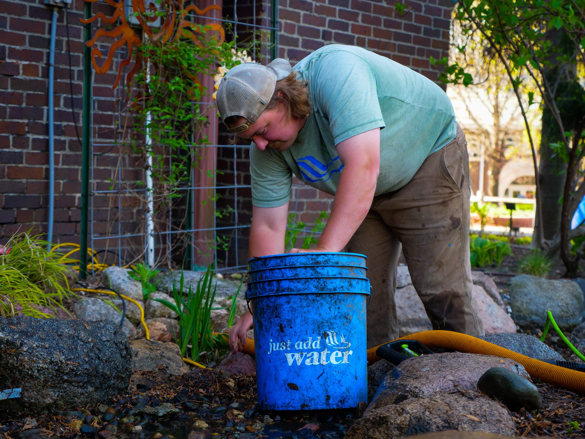 Just Add Water technician cleaning a pond edge beside a branded blue bucket