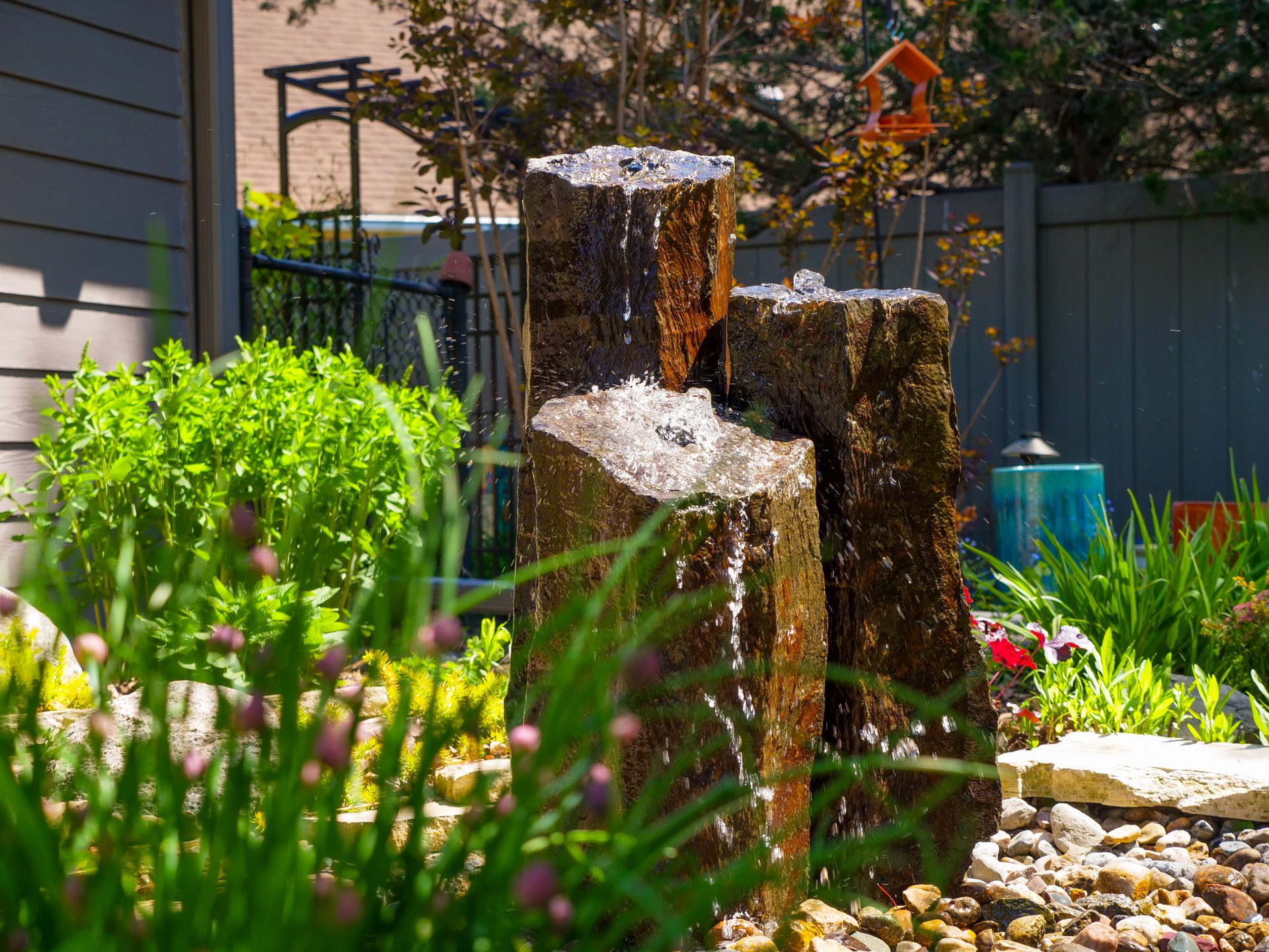 Basalt column fountain spilling water into a bed of river rock and garden plants