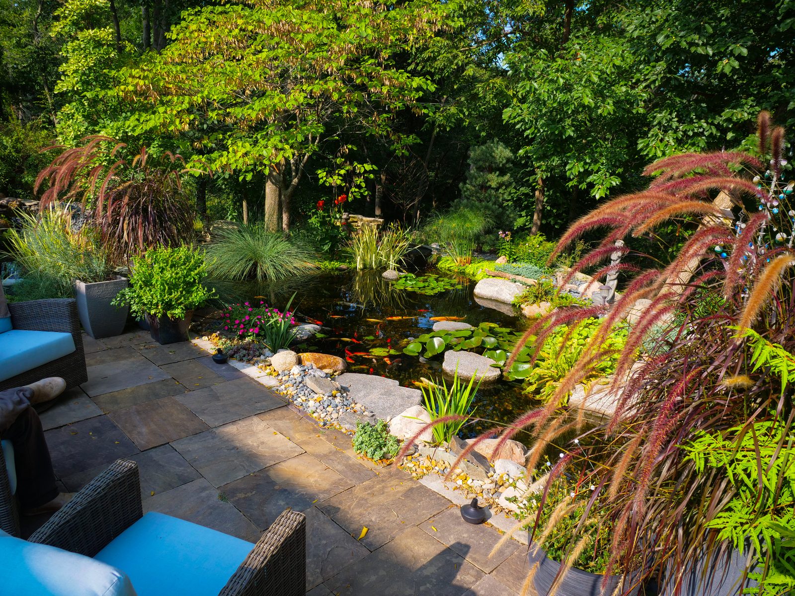 Stone patio with ornamental grasses beside a pond filled with lily pads