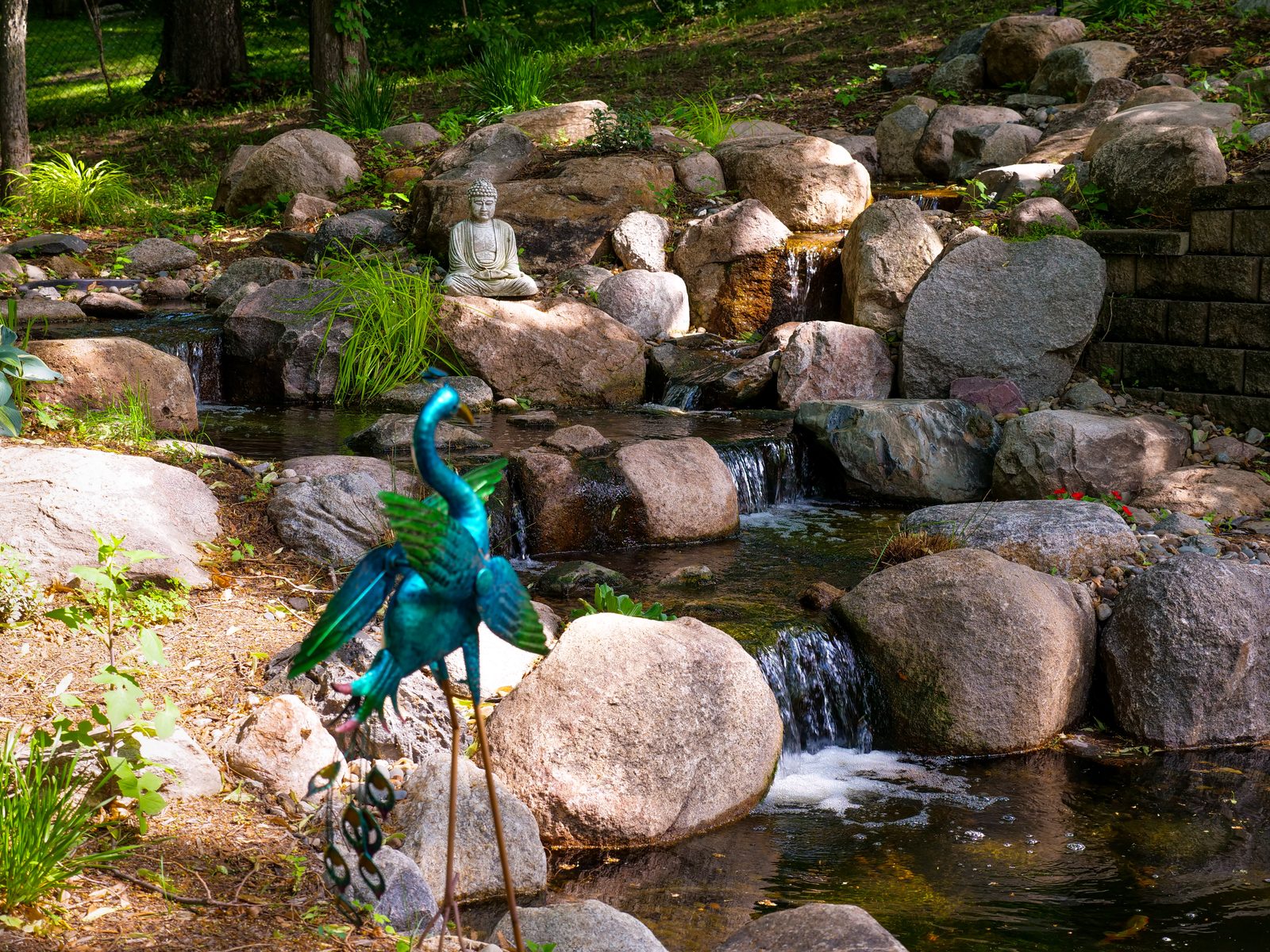 Fountain feature spilling over boulders past a stone garden statue