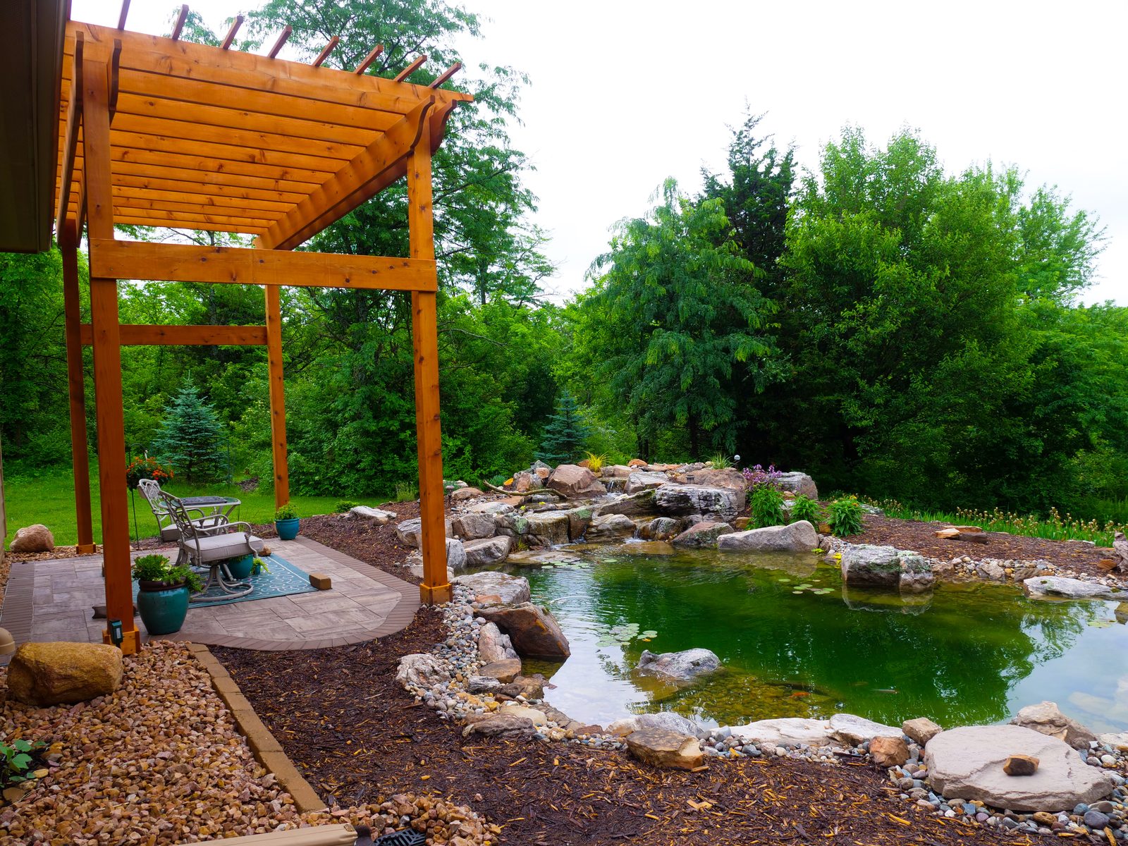 Backyard pond with a waterfall next to a cedar pergola with patio seating