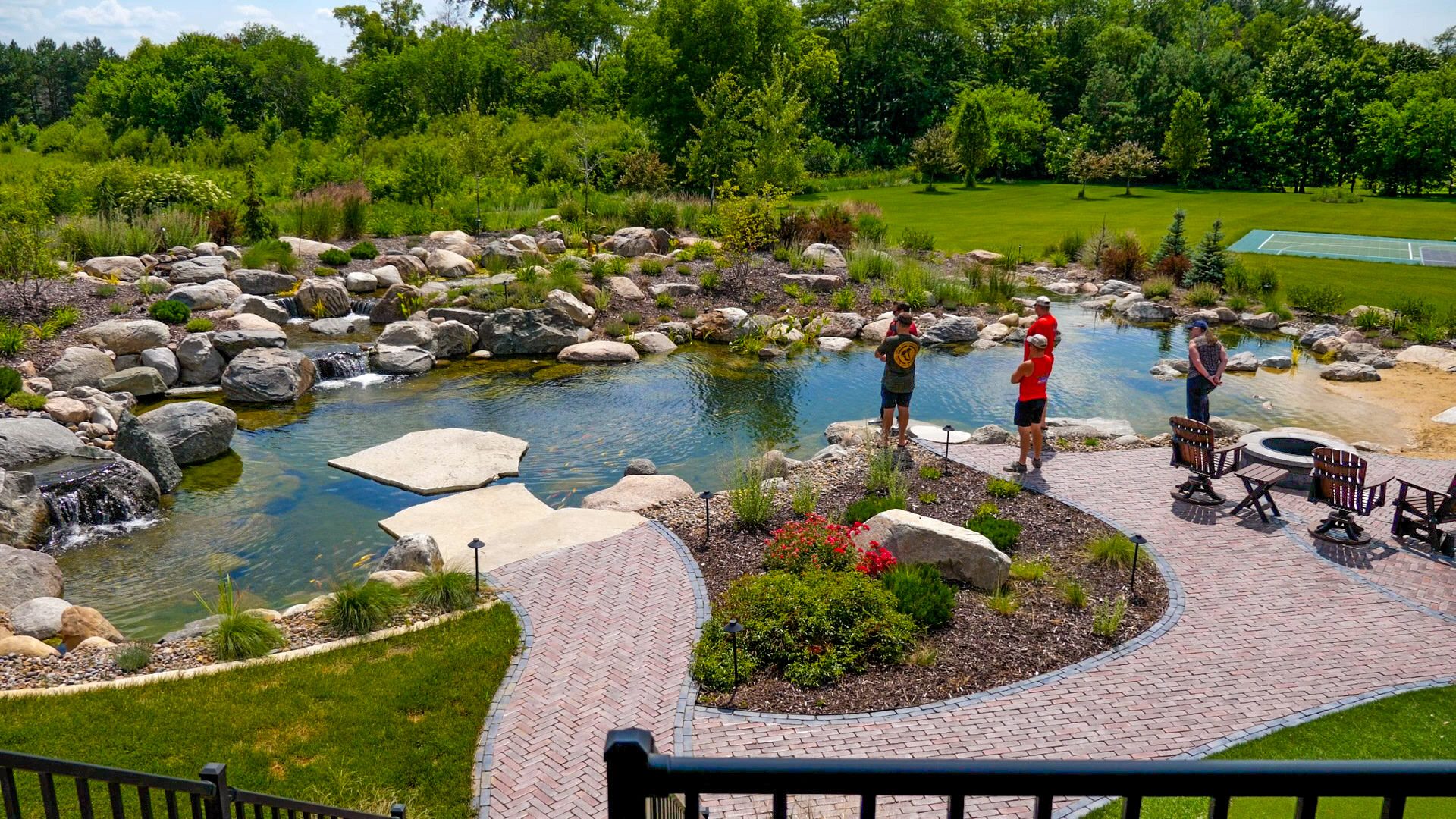 Large recreational pond with a brick patio, fire pit, and guests gathered at the water's edge