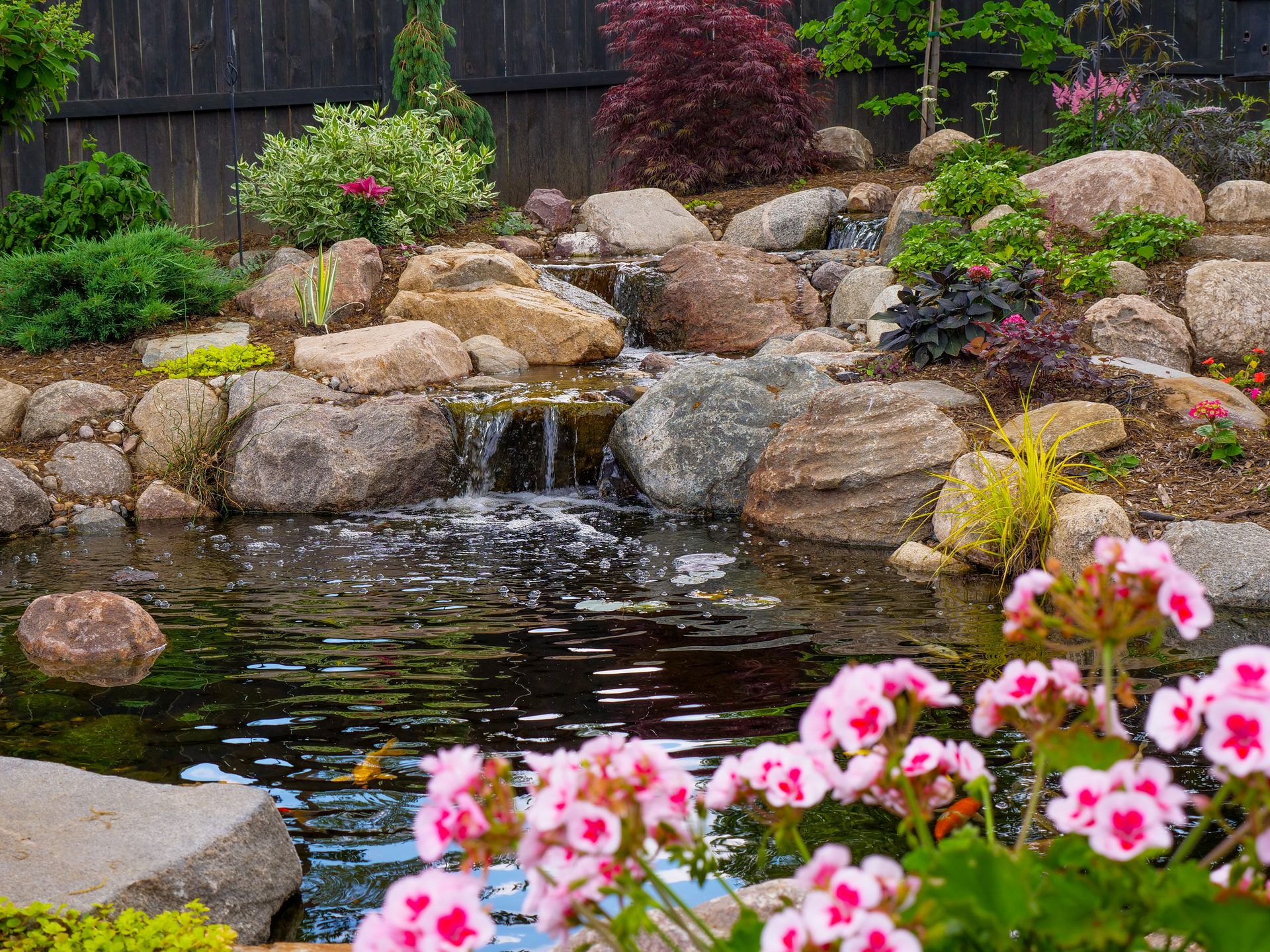 Multi-drop waterfall spilling into a pond surrounded by pink blooms