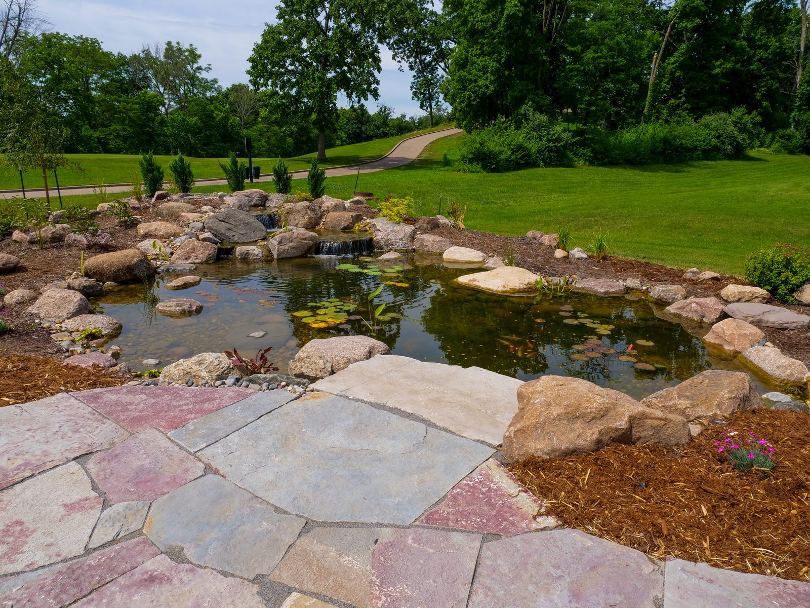 Recreational pond edged with boulders and a flagstone patio in a green lawn