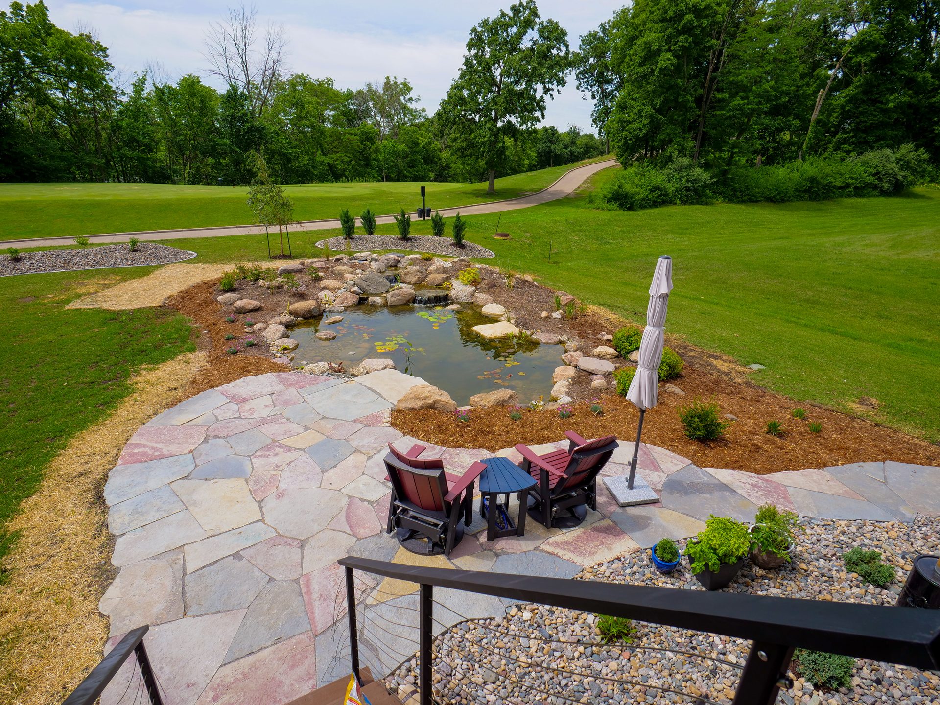 Recreational pond with a flagstone patio, seating, and open lawn beyond