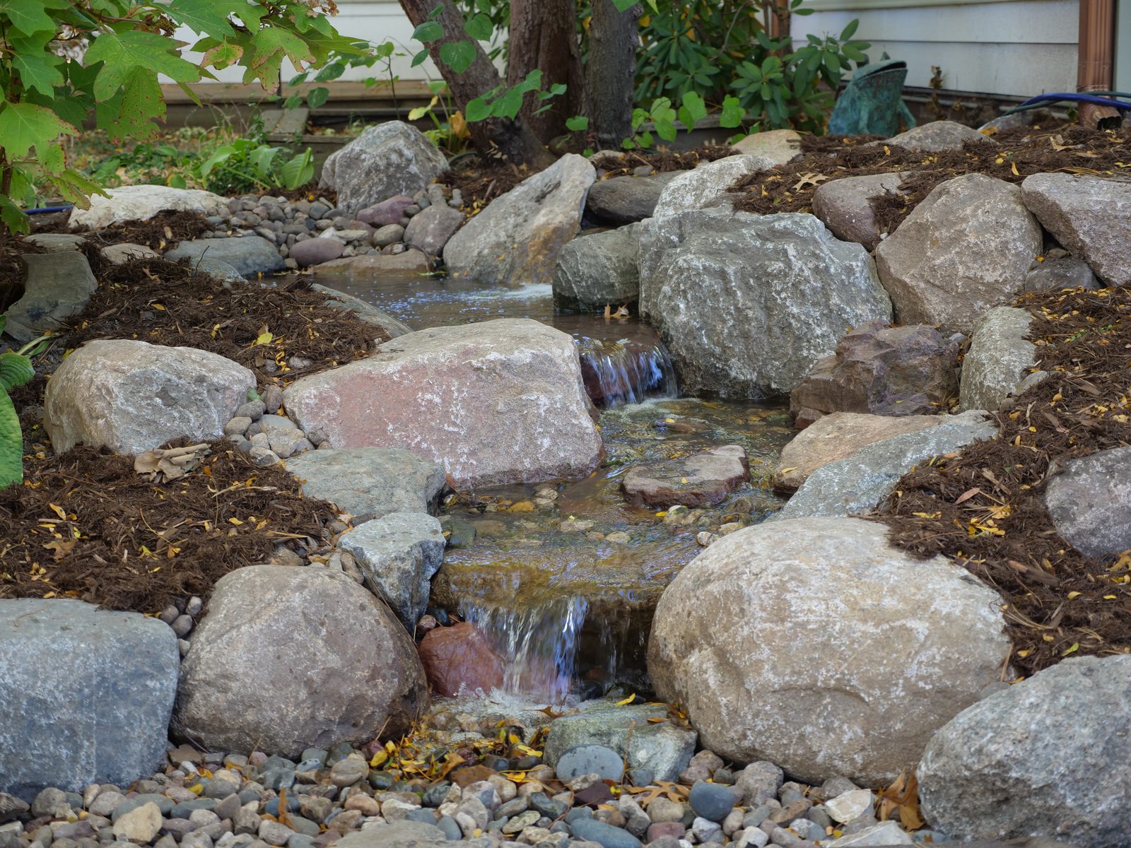 Freshly built stone stream lined with boulders and mulch beside a home