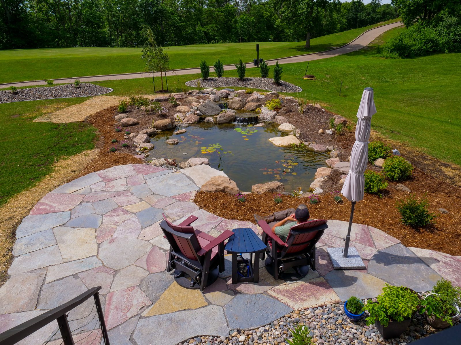 Aerial view of a recreational pond with a flagstone patio and seating beside a golf course